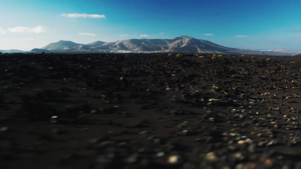 Zwart lavaveld met vulkanen en een wit dorpje op Lanzarote