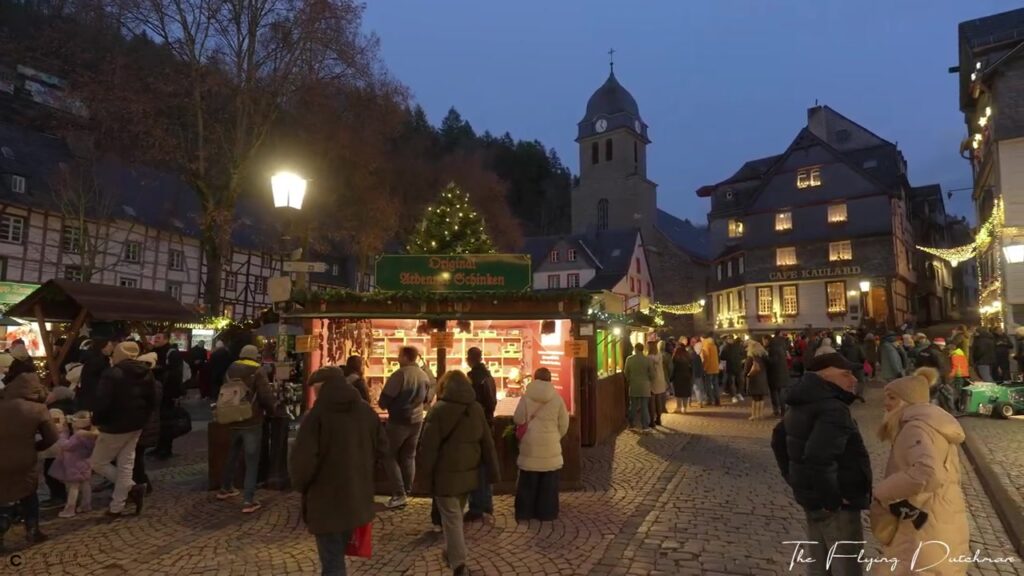 Kerstmarkt in Monschau met vakwerkhuizen en een kerktoren in de avond